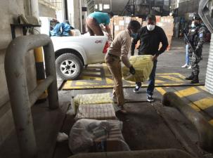    Illegal drugs are being confiscated in Ecuador. Packets are being loaded from a white pickup truck into a loading bay by three men wearing masks.