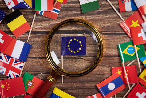 A magnifying glass sits on the flag of European Union in a circle of other flags from around the world