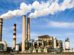 Energy producing factory with 4 tall chimneys , 2 are releasing vast clouds of white vapour under a blue sky with white clouds