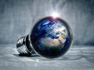 The planet Earth sits inside a light bulb resting on its side. The bulb sits in an empty grey space