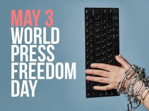 Black keyboard with a chained white hand on top of it with a blue background | World Press Freedom Day is written on the left side in large pink and white letters