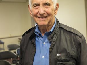 Image of Daniel Ellsberg U.S. whistle-blower. A senior white male smiles warmly into the camera wearing a white shirt and black jacket.