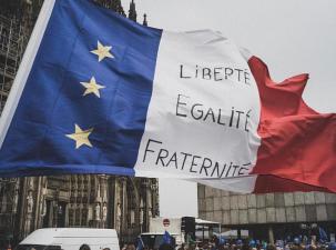 The Feench flag is held up high in a square with the words 'liberte, egalite, and fraternite' written on it