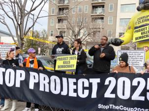 Protesters rally infront of the Heritage Foundation building in Washington DC. The hold a large black banner that says 'Stop Project 2025'