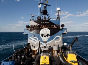 Sea Shepherd anti-whaling team stand on the bridge of one of their ships with the skull logo painted behind them