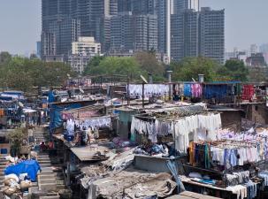 Image of a slum in India with many clothes hanging out to dry, in the background is a modern city with many skyscrapers.