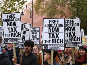 Protesters stand in a green park holding signs calling for free education and a tax on the rich