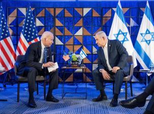 President Joe Biden meets with Prime Minister Benjamin Netanyahu, they are leaning in to each other and sitting in front of their countries flags