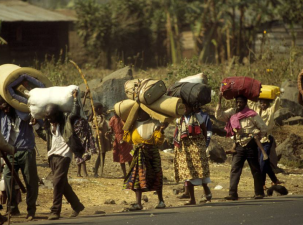 A stream of refugees walk along the road carrying all their possessions