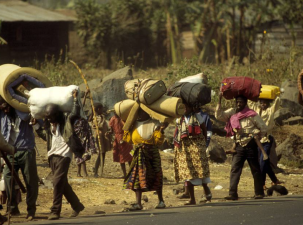 A stream of refugees walk along the road carrying all their possessions 