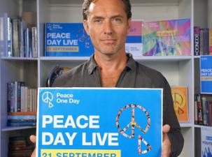 Jude Law, Peace One Day ambassador holds up a sign with the details of the 2025 Peace One Day Campaign.