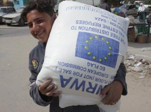 A young UNRWA worker carries a large white sack of flour helping to support Palestinian refugees