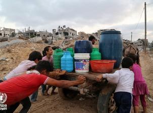Children help to push a wooden cart in Gaza carrying buckets of water.