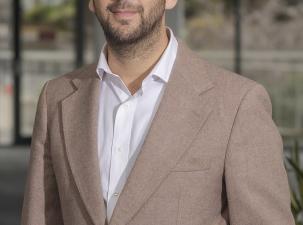 Leader of the Green Party Zack Polanski poses for a portrait wearing a beige suit and white shirt.