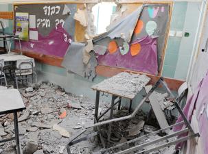 A kindergarten classroom in Gaza has been destroyed by a bomb. There is rubble everywhere and there is a huge hole in the wall.