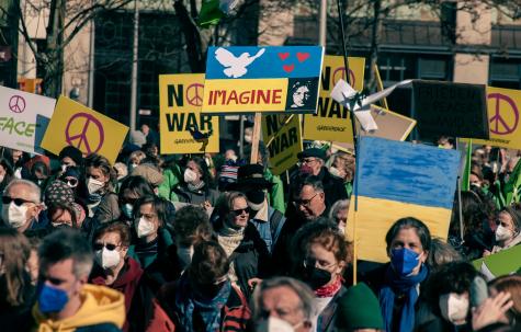 Many anti-war protesters stand in the street holding placards with the blue and yellow Ukraine flag and words of No War written across them