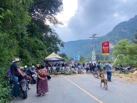 Many protesters in Guatemala gather at a roadblock made from cut down trees, rope, and large rocks