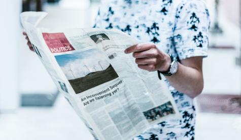 Close-up of a man wearing a blue and white beach shirt holding an open newspaper