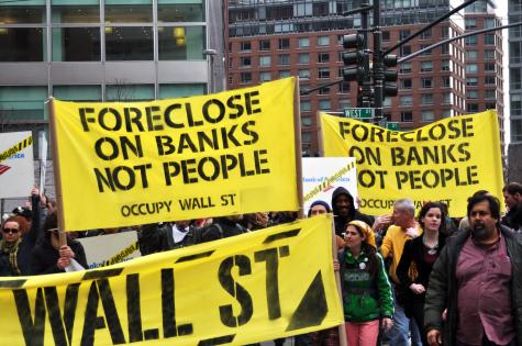 Protesters carry bright yellow posters at an Occupy Wall Street March in 2012. The signs read 'Foreclose on banks not people'