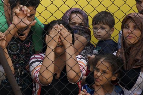 Syrian refugees, men, women, and children, stand behind a fence in dispair in Budapest, Hungary.