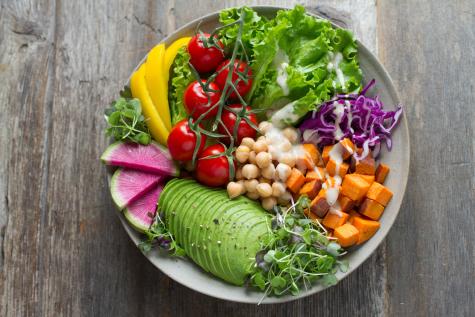 A huge bowl of colourful vegatables sits on a grey table. 