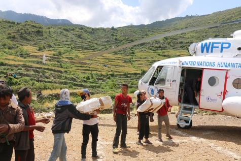 A white United Nations World Food Progam plane arrives bringing humanitarian supplies into Nepal. People help unloading the sacks