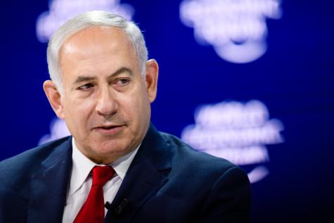 Benjamin Netanyahu, Prime Minister of Israel during the WEF conference in Davos in 2018. He wears a black suit and red tie infront of a blue background looking away from the camera 