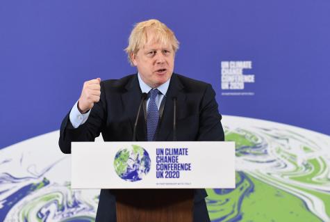 Boris Johnson at the launch of COP26. The British PM at the time stands behind a podium with his fist in the air. A huge blue COP 26 banner is behind him