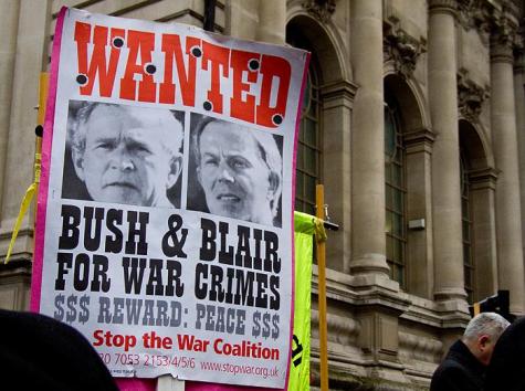 A large 'Wanted' poster is on display at an anti-war protest. The images of Tony Blair and George Bush are displayed with the words 'Bush and Blair wanted for war crimes'