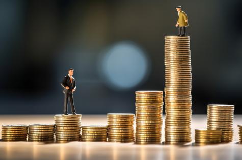 Two small figurines stand on top of different sized stacks of coins representing economic inequality in the real world