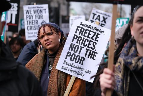 A protester opposite Downing Street listens to one of the speakers on a day of action over the surging cost of living. She holds a sign which reads 'Freeze Prices - Not the Poor'