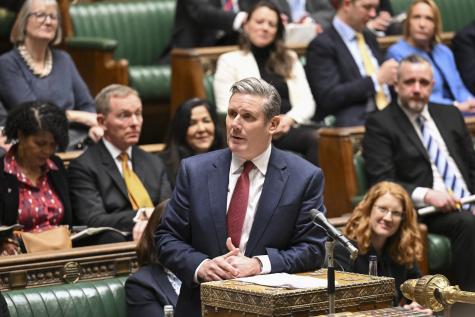 Keir Starmer the leader of the UK Labour Party stands in the House of Commons infront of a microphone wearing a blue suit and red tie 