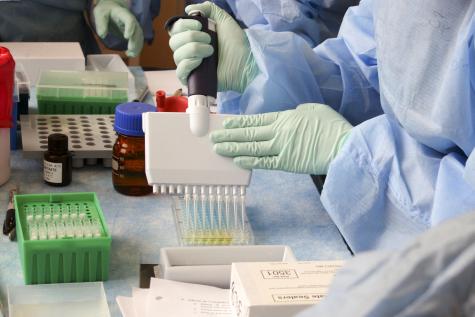 Close up image of two people wearing protective gear and latex gloves using trsting equipment in a laboratory 