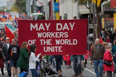 May Day March in Melbourne, Australia. Protesters hold up a large red sign that says 'Workers of the World Unite.'