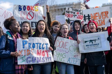 A group of students are outside protesting against violence and guns in schools, they hold signs which say 'An assault on our future' and 'Protect kids not guns' 