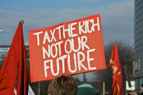 A protester holds a large orange sign which says 'Tax the rich not our future'