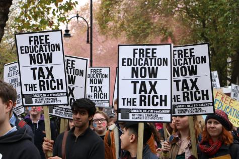 Protesters stand in a green park holding signs calling for free education and a tax on the rich