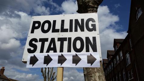 A large white sign is attached to a post signaling the way to a polling station