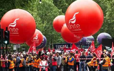 Unite protesters gather at a demonstration for better pay and conditions. There are huge red balls which say Unite in the air and many people are holding Unite banners and flags