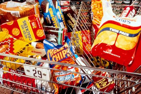 A shopping cart in a supermarket is filled to the brim with chocolate, crisps, sweets, and biscuits