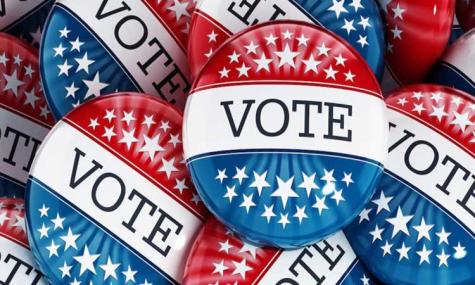 Red, white, and blue badges sit in a pile with the word 'Vote' written in large letters across the centre.