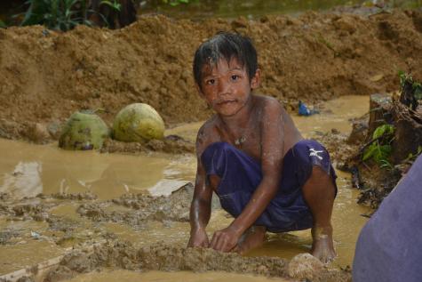 A very young boy wear shorts and no shirt crouches down in a pool of water searching for gold at a mine in the Philippines.