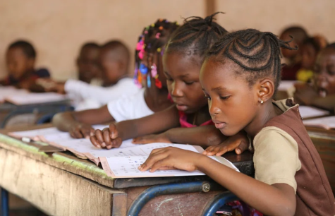 Young girls in Mali are in a classroom working on a wooden desk looking at a book