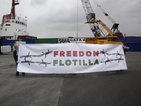 A huge Freedom Flotilla banner is held up in front of a large ship which says Gaza on it