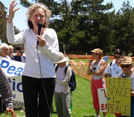 Kathy Kelly holds a microphone giving a speech at a peace rally