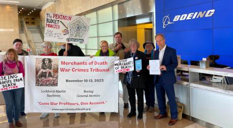 Image of the subpoena being delivered to Boeing corporation. Activists stand in the lobby holding large banners and the document.