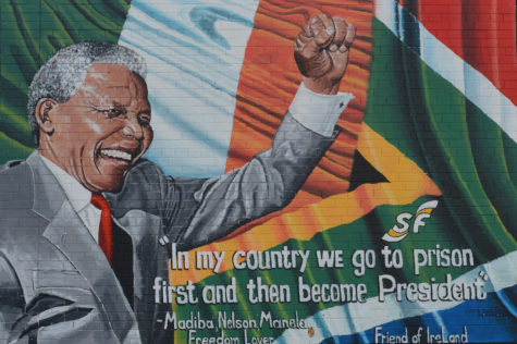 Colourful mural of Nelson Mandela painted in Ireland. Wearing a suit he holds his fist in the air. The words 'In my country we go to prison first and then we become President' are written below.