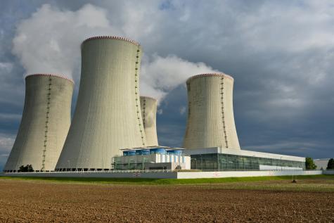 Image of four huge white cooling towers at a nuclear power plant in the Czech Republic. White steam clouds rise into the sky above them.