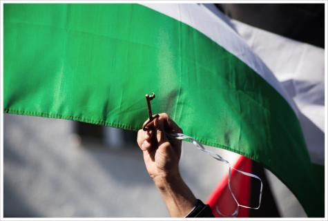 A Palestinian flag waves in the wind while someone holds a golden key beneath it