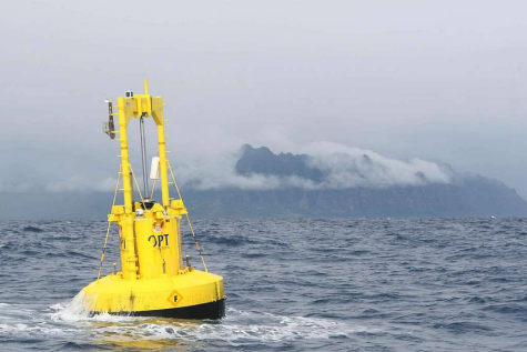 A yellow wave energy buoy floats off the east coast of Hawaii. There are cloudy mountains in the background